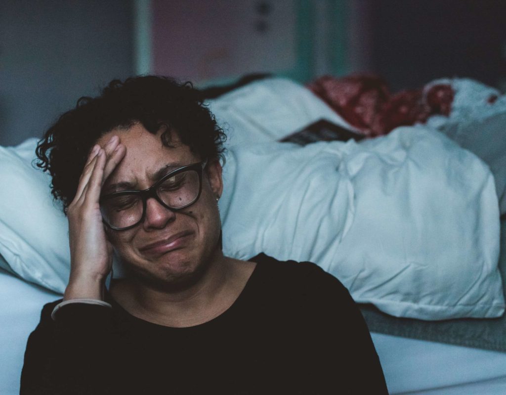 A young black woman crying beside her bed