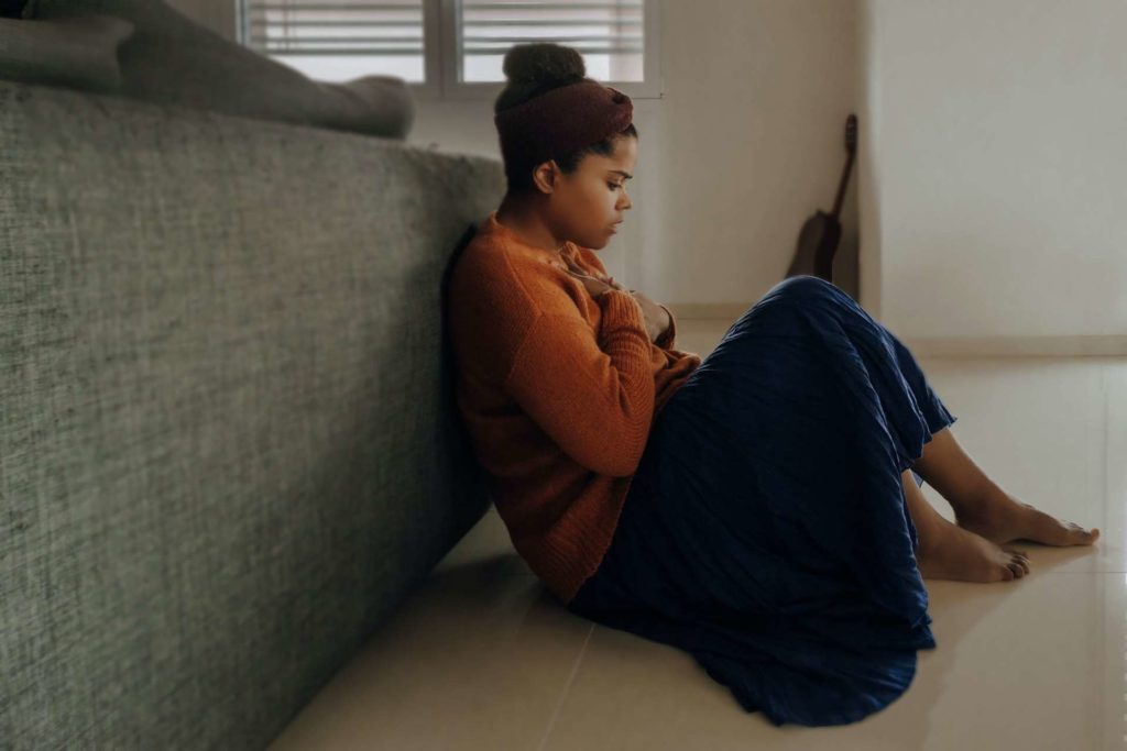 A young black woman sitting against the back of a couch holding her chest