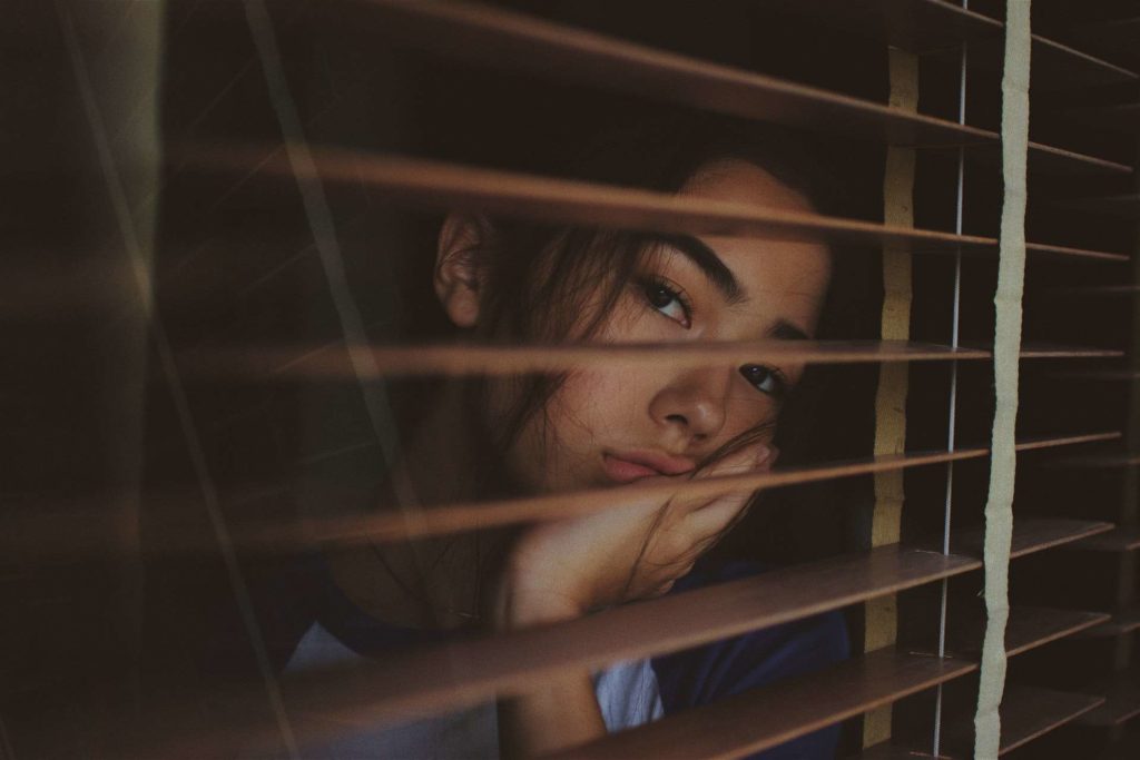 A sad Asian woman looking out window blinds