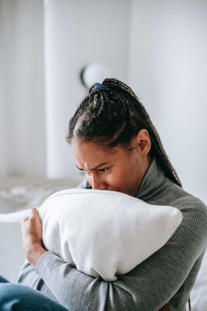 A sad young black woman holding a white pillow tightly