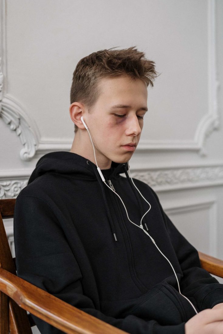 A young teen boy with a black eye and earbuds in his ears