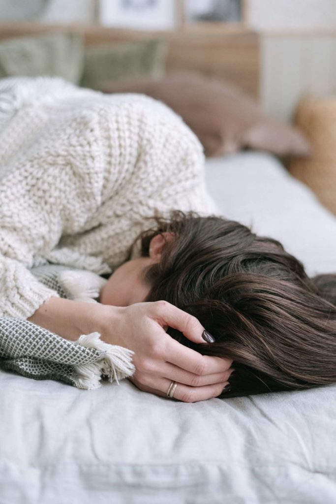 A young white woman laying on a bed covering her face with her hand and wrist