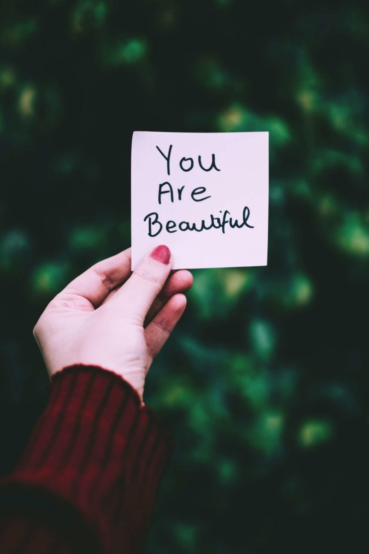 A woman's hand holding a sticky note that says "You are beautiful"