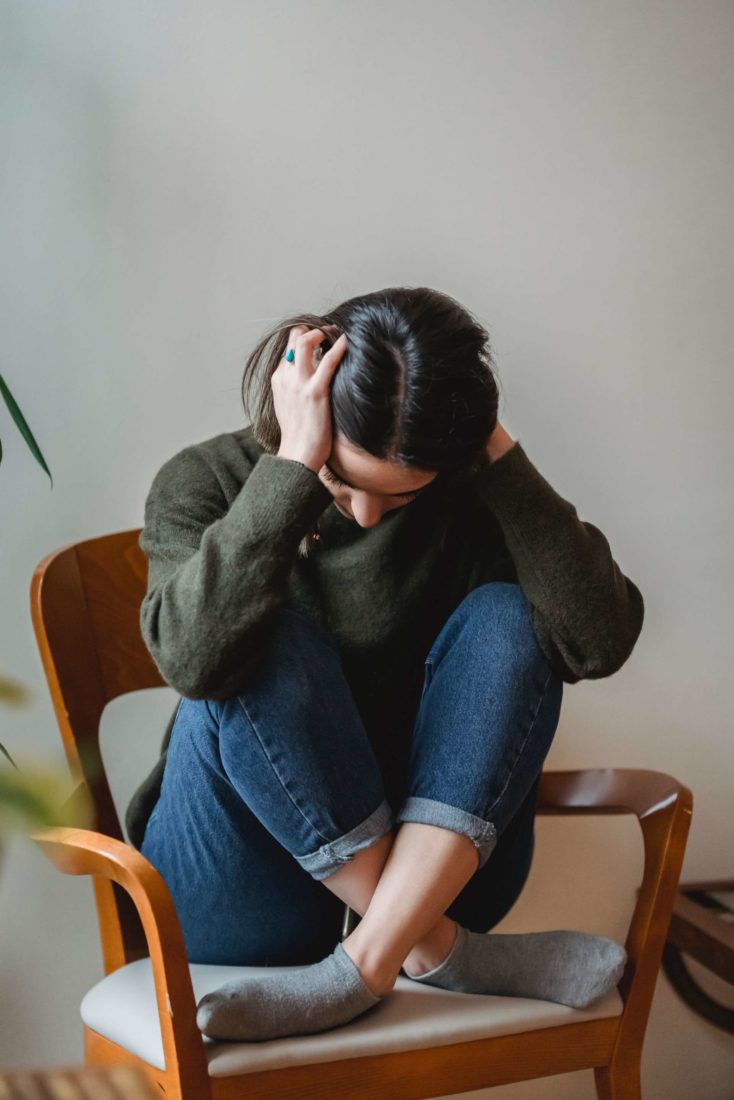 An upset young woman holding her head while sitting in a chair and her legs criss crossed