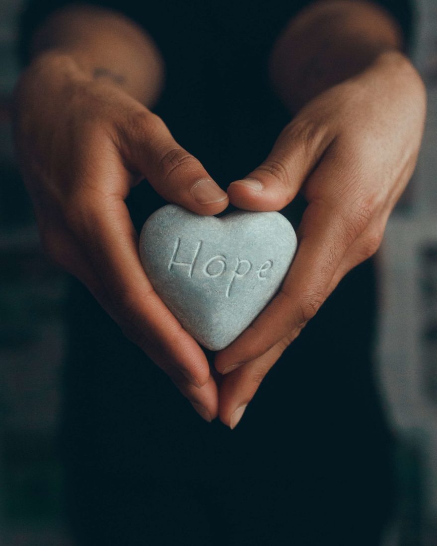 A person's hands holding a stone that says "Hope"