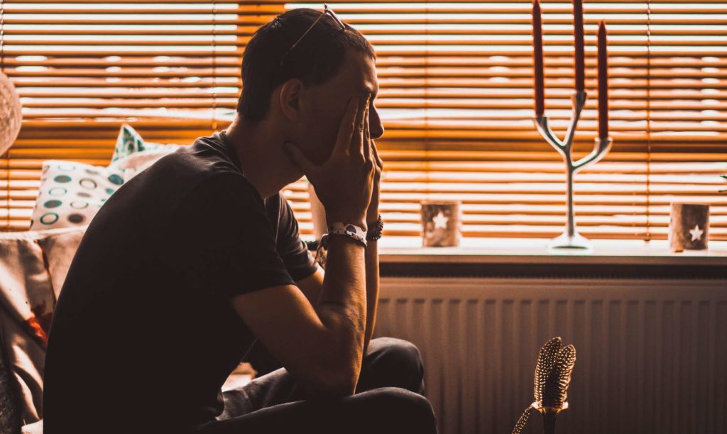 A man with his hands over his eyes sitting in a room