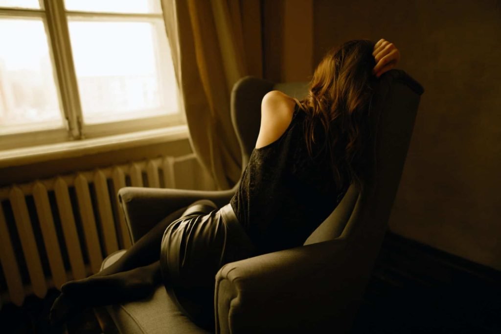 A sad woman curled up in a chair by a window
