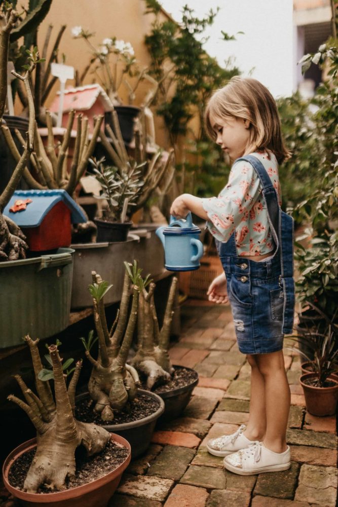 A young white girl watering a garden
