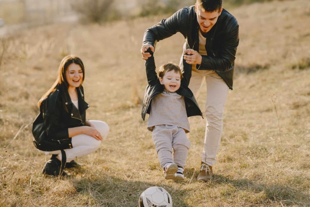 A young father holding his son by his hands while his mother looks on