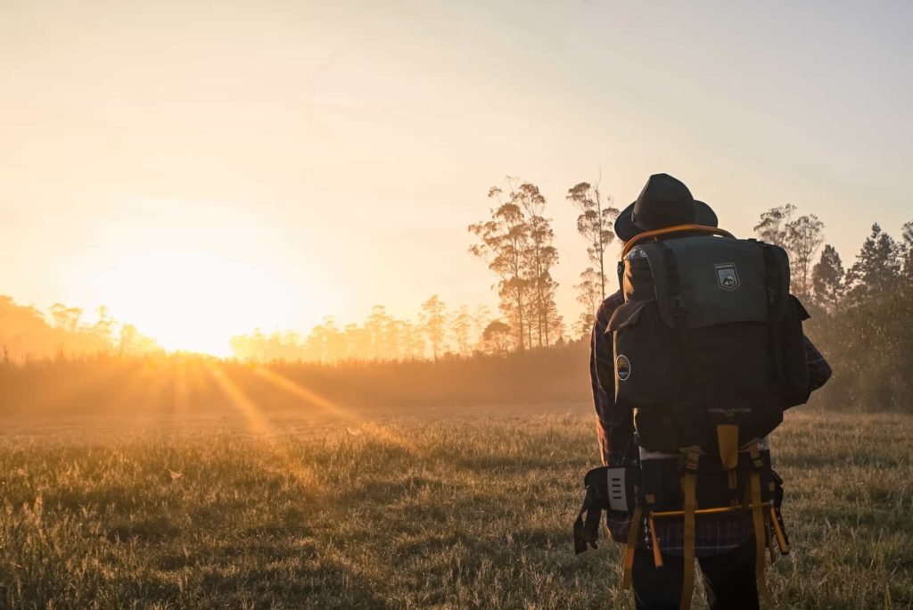 A person with a backpack looking toward the sun at sunset