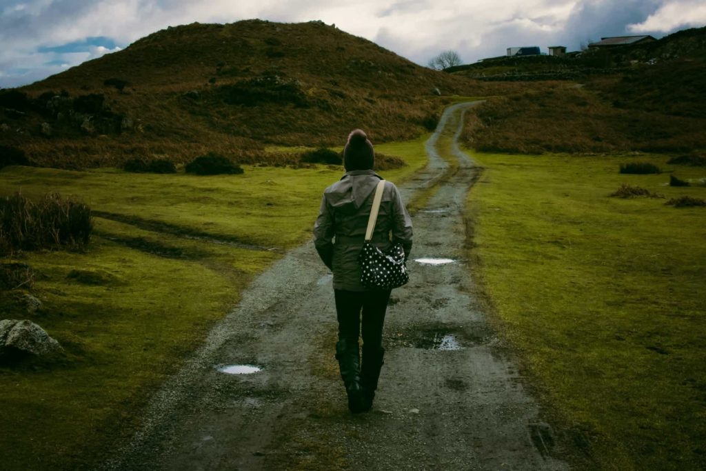 A person walking down a dirt path through the hills