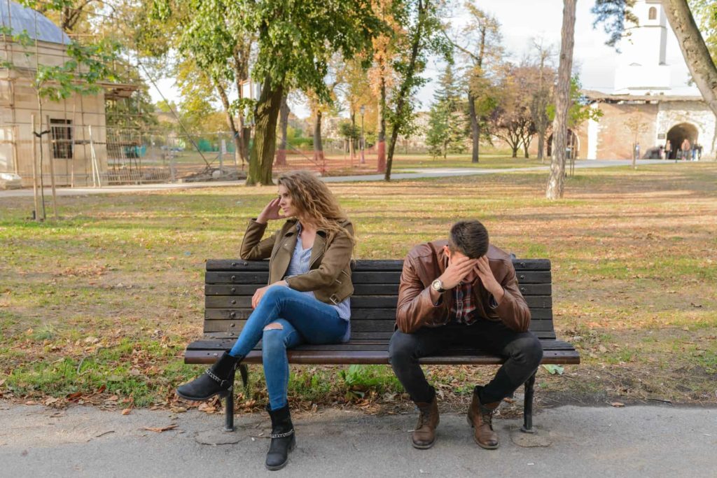 A frustrated couple sitting on a park bench facing away from each other