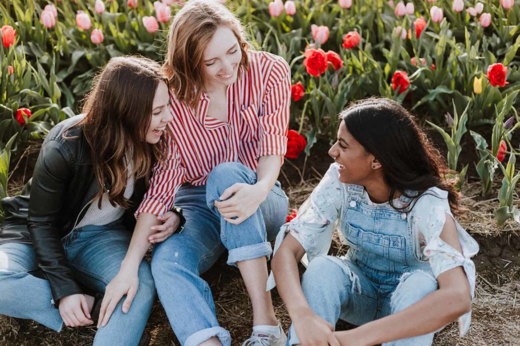 A group of young woman laughing on the ground near some flowers