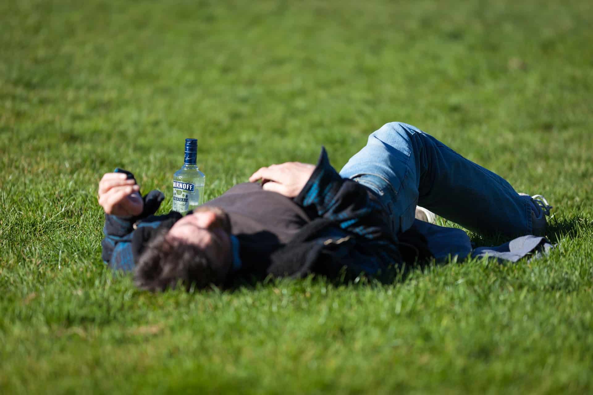 A white man passed out in the grass by a liquor bottle