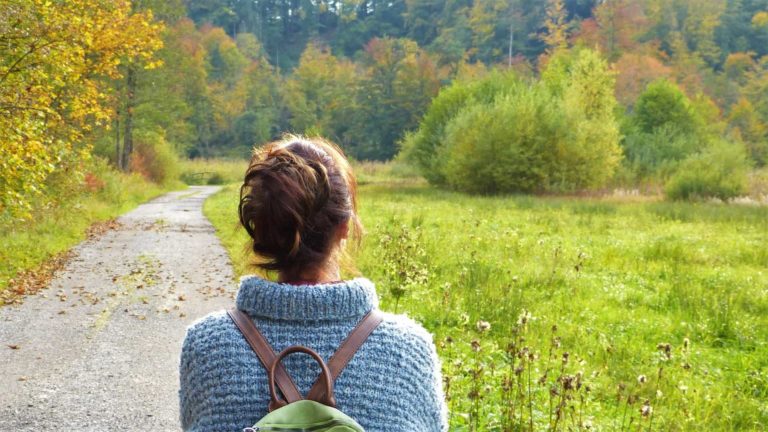 A young woman with a backpack on a path looking off into the forest