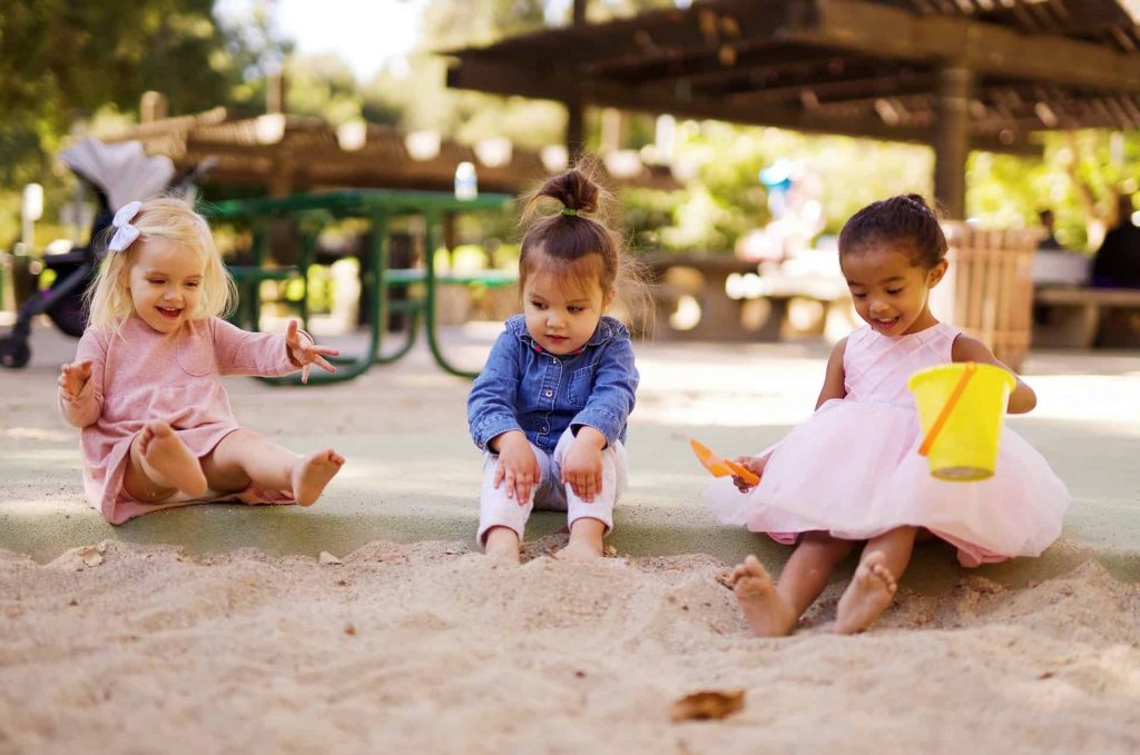 Three young children playing in a sandbox