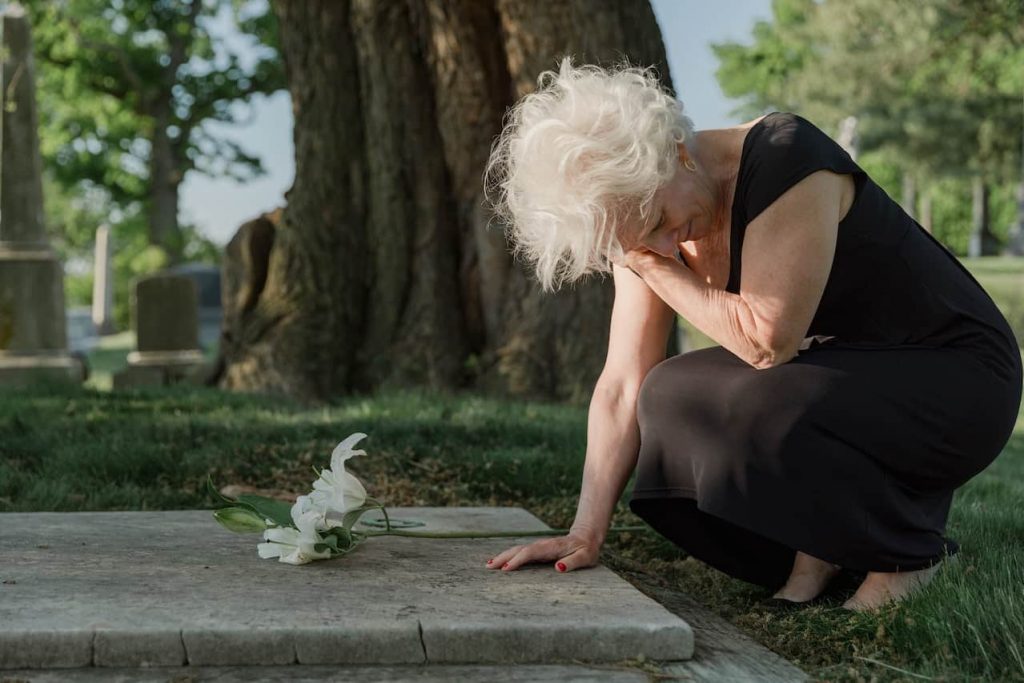 An older woman kneeling down and crying over a grave