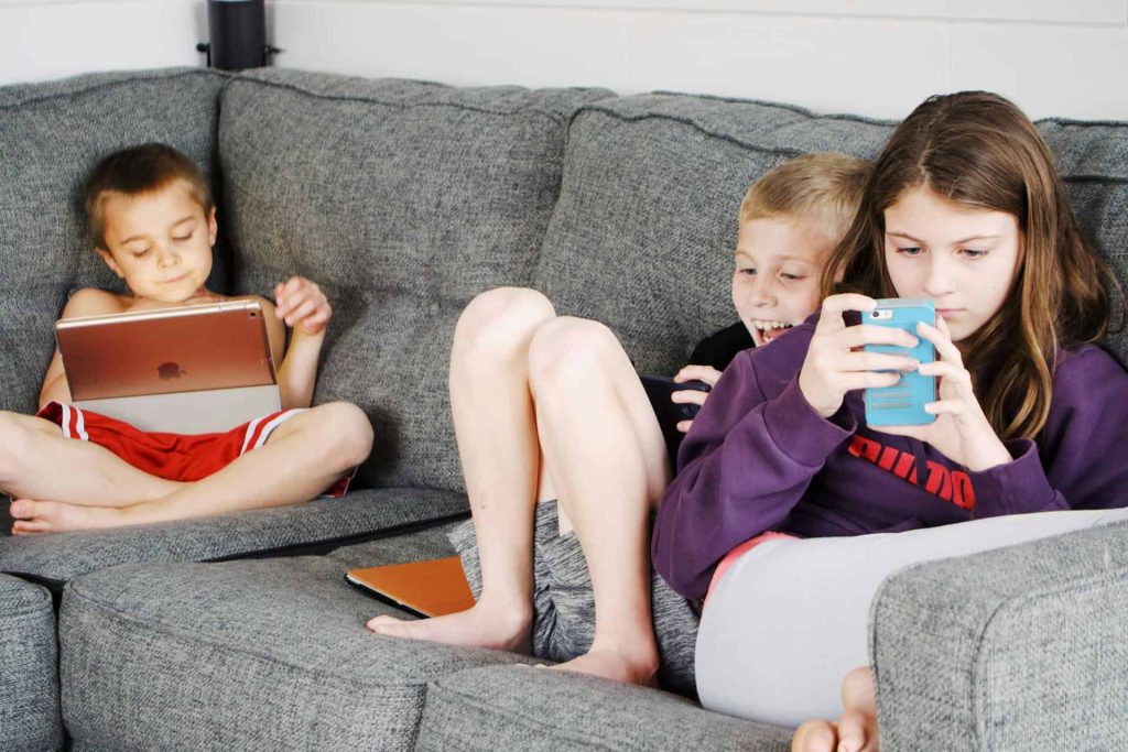 One girl and two boys engrossed in their electronic devices