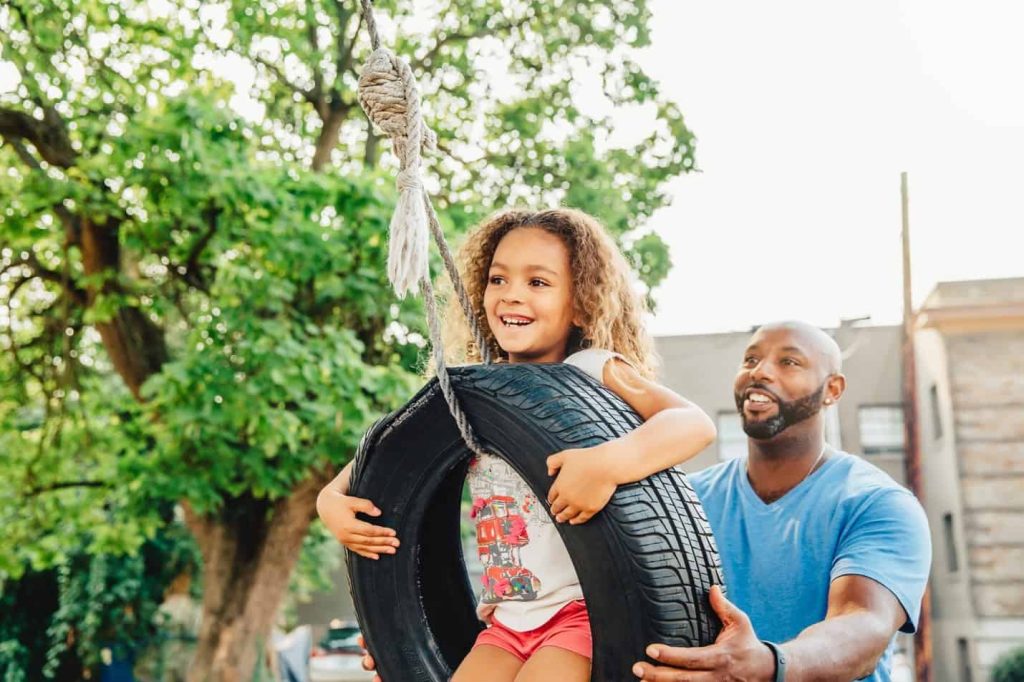 A mixed race girl being pushed on a tire swing by her dad