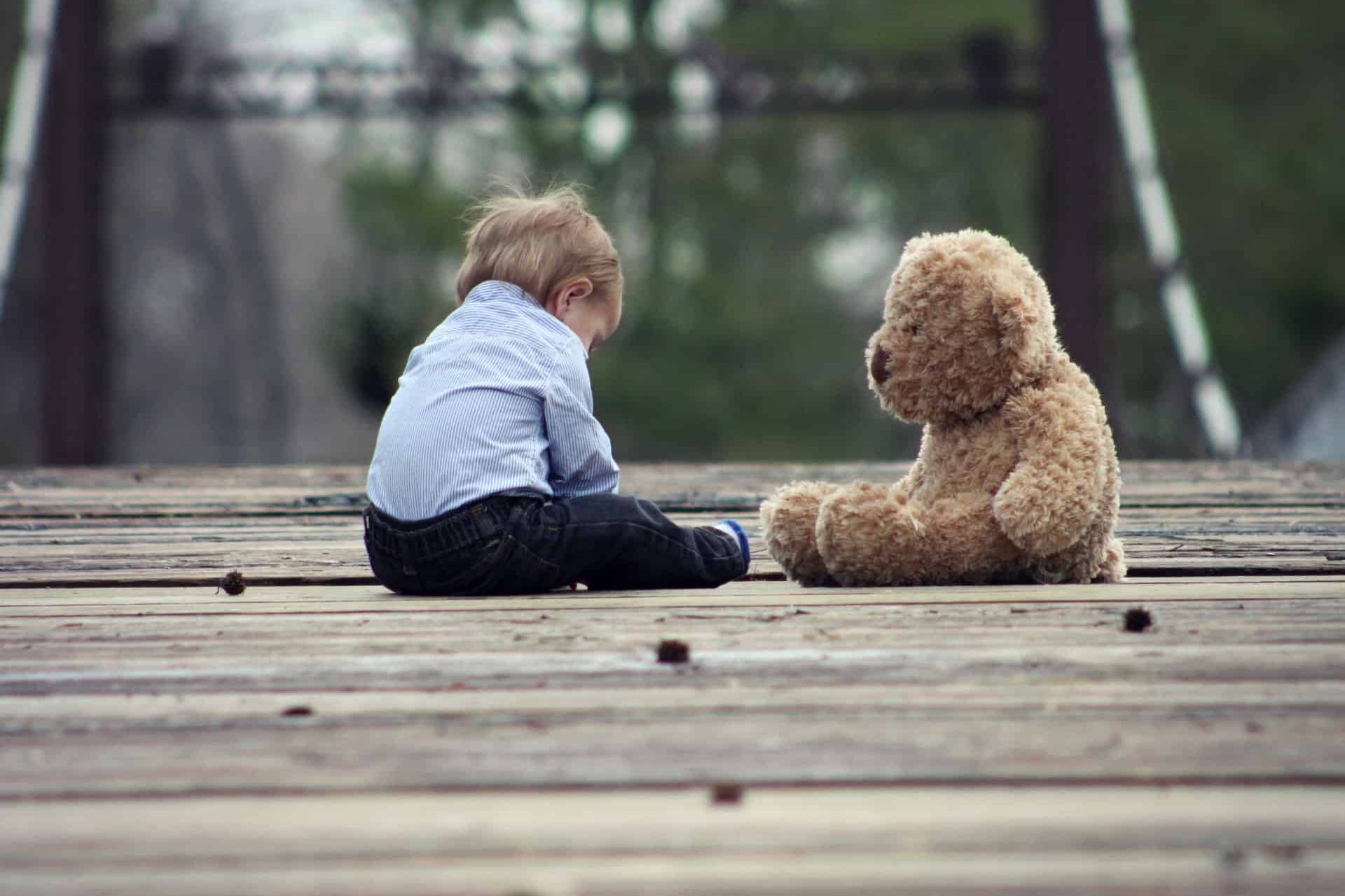 A young boy with his teddy bear on a wooden bridge
